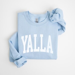 May include: A light blue sweatshirt with the word "YALLA" printed in white on the front.