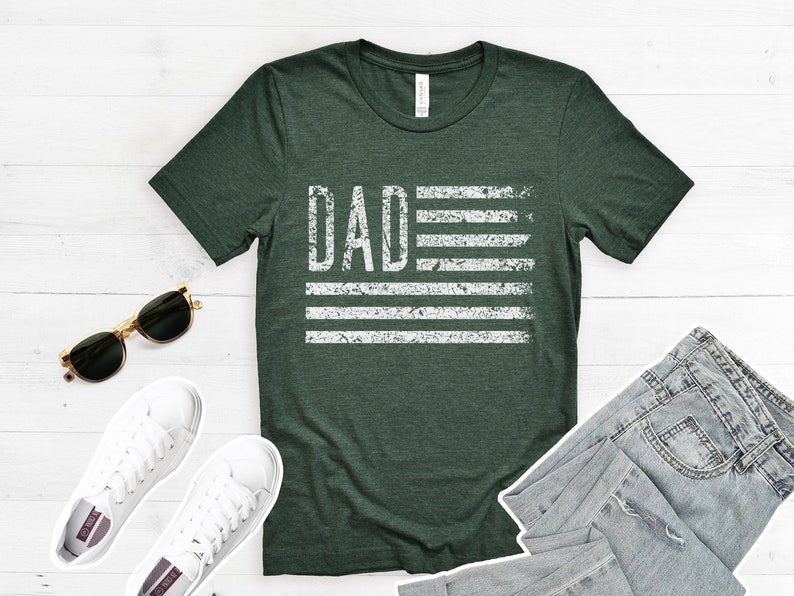 May include: A dark green t-shirt with a white distressed graphic of an American flag with the word "DAD" in place of the stars.