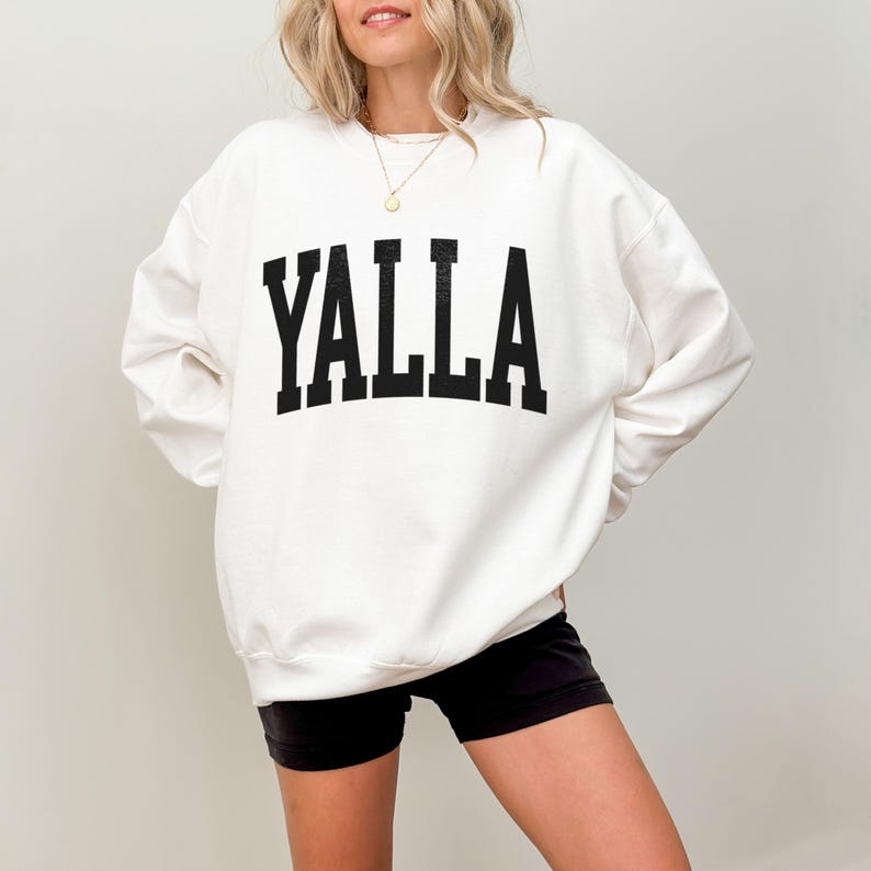 May include: White sweatshirt with black text that reads "YALLA" in a collegiate font.