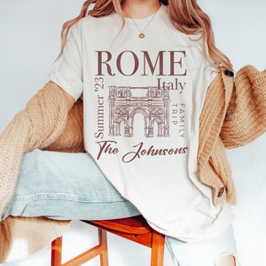 May include: A white t-shirt with a brown graphic of the Roman Colosseum and the text "ROME Italy Family Trip Summer '23 The Johnsons".