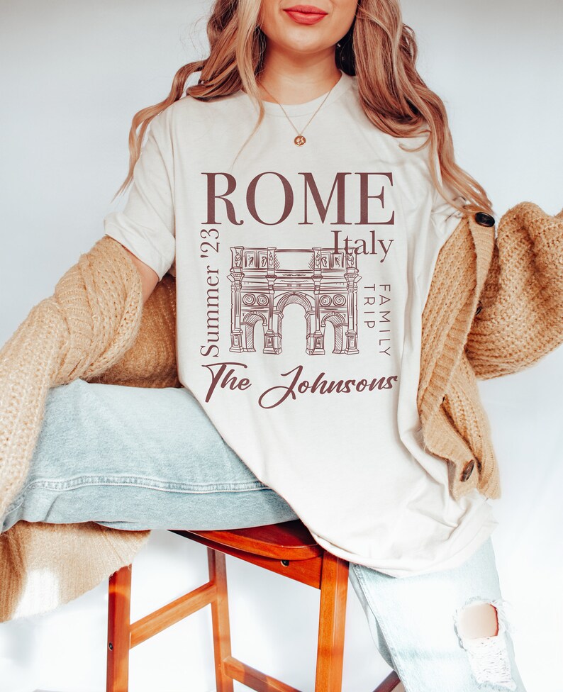 May include: A white t-shirt with a brown graphic of the Roman Colosseum and the text "ROME Italy Family Trip Summer '23 The Johnsons".