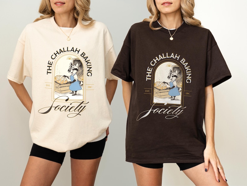 K&ouml;nnte beinhalten: Zwei T-Shirts, eines in Creme und eines in Braun, mit einer Grafik eines B&auml;ckerracoon und dem Text "The Challah Baking Society". Das Design beinhaltet ein bogenf&ouml;rmiges Fenster und das Wort "Society" in Schreibschrift. Die Shirts sind kurz&auml;rmelig.