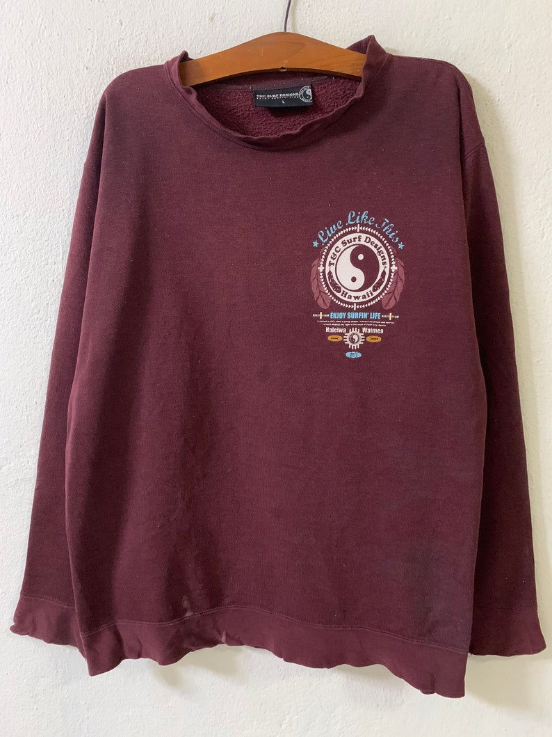 Puede incluir: Sudadera color burdeos con un estampado gr&aacute;fico de un s&iacute;mbolo yin yang con el texto "Live Like This" y "TGC Surf Designs Hawaii" alrededor.