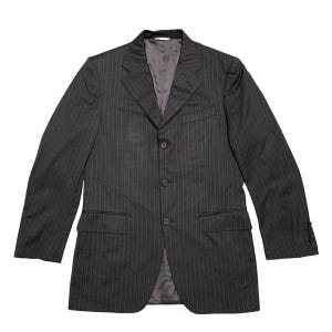 Puede incluir: Una chaqueta de traje gris oscuro con rayas finas, cierre de un solo botón y tres botones. La chaqueta tiene solapa de muesca y dos bolsillos de solapa.