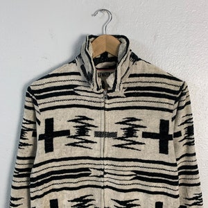 Puede incluir: Una chaqueta con cremallera de color crema con un patr&oacute;n geom&eacute;trico en blanco y negro. La chaqueta tiene un cuello alto y una cremallera. El nombre de la marca "LITWATER" es visible en la parte delantera de la chaqueta.