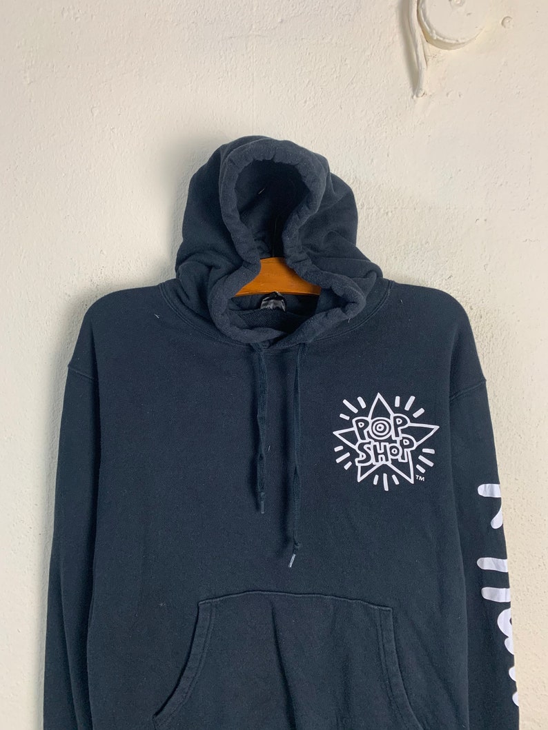 May include: Black hooded sweatshirt with a white starburst graphic featuring the text "Pop Shop" and a trademark symbol. The left sleeve has a white graphic with the text "Pop Shop" repeated vertically.