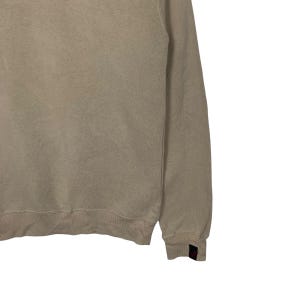 May include: A light beige sweatshirt with long sleeves and a crew neck. The sweatshirt is made of a soft, comfortable fabric.