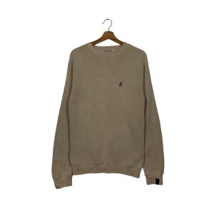 May include: A beige sweatshirt with a small black logo on the front.