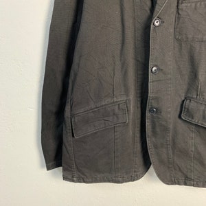 Puede incluir: Un blazer gris oscuro con cierre de dos botones, solapas con muescas y m&uacute;ltiples bolsillos. La chaqueta tiene un corte entallado y est&aacute; hecha de una tela texturizada. Una prenda de vestir cl&aacute;sica.