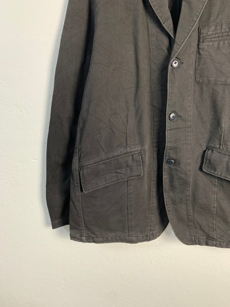 Puede incluir: Un blazer gris oscuro con cierre de dos botones, solapas con muescas y m&uacute;ltiples bolsillos. La chaqueta tiene un corte entallado y est&aacute; hecha de una tela texturizada. Una prenda de vestir cl&aacute;sica.