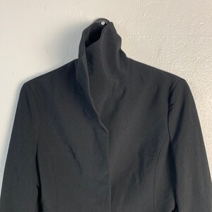 May include: A black blazer with a high, folded collar. The blazer has a single button closure and long sleeves.