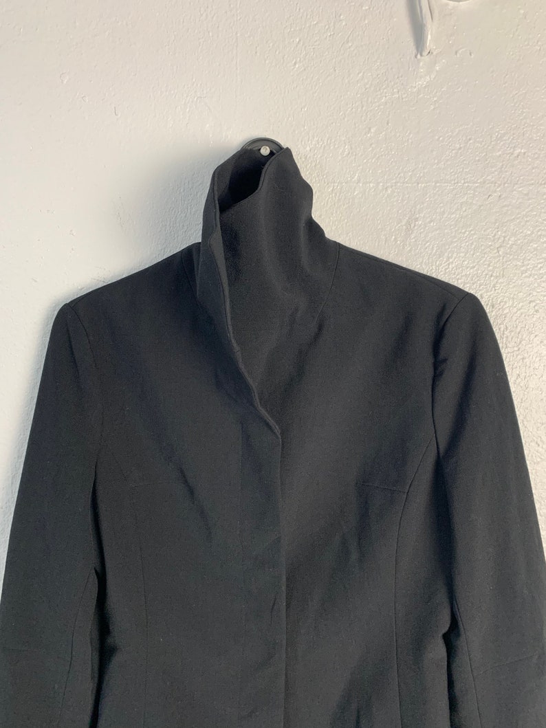 May include: A black blazer with a high, folded collar. The blazer has a single button closure and long sleeves.