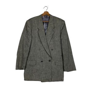 Puede incluir: Una chaqueta gris de doble botonadura con un patrón texturizado. La chaqueta tiene solapa de muesca y cuatro botones.