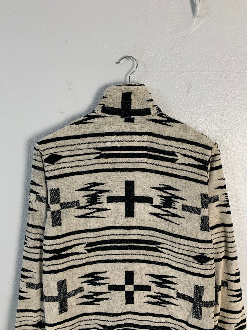 Puede incluir: Un su&eacute;ter de manga larga beige y negro con un patr&oacute;n geom&eacute;trico de cruces y flechas.
