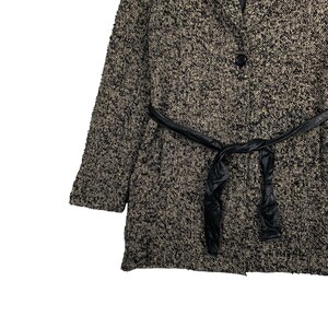 Puede incluir: Un abrigo texturizado negro y beige con cintur&oacute;n de cuero negro. El abrigo tiene un cierre de un solo bot&oacute;n y un dise&ntilde;o cl&aacute;sico. La tela parece ser un material tejido, adecuado para climas m&aacute;s fr&iacute;os.