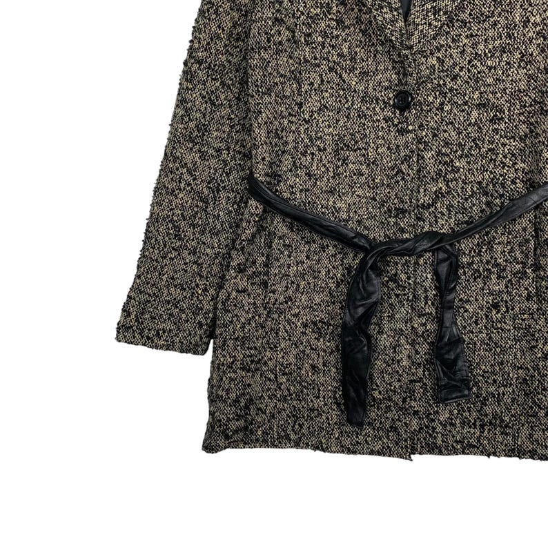 Puede incluir: Un abrigo texturizado negro y beige con cintur&oacute;n de cuero negro. El abrigo tiene un cierre de un solo bot&oacute;n y un dise&ntilde;o cl&aacute;sico. La tela parece ser un material tejido, adecuado para climas m&aacute;s fr&iacute;os.