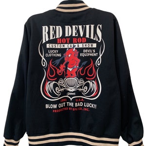 Könnte beinhalten: Schwarze Bomberjacke mit einem roten, weißen und schwarzen Grafikdruck eines Cartoon-Teufels, der einen Hot Rod fährt. Der Text "Red Devils Hot Rod Custom Cap & Show" ist auf der Jacke aufgedruckt. Der Text "Lucky Clothing Devil's Equipment" ist unter dem Grafikdruck aufgedruckt. Der Text "1991 U.S.A. Blow Out The Bad Luck!! Produced by Efu Co., Inc." ist unter dem Grafikdruck aufgedruckt.