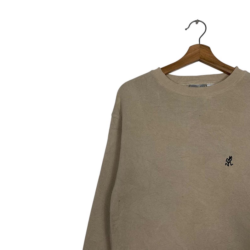 May include: A beige sweatshirt with a small black graphic on the right side of the chest.