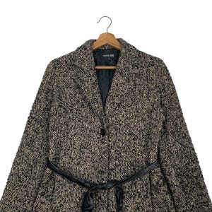 Puede incluir: Un abrigo de tweed negro y beige con cintur&oacute;n de cuero negro. El abrigo tiene cuello con solapas, cierre de un solo bot&oacute;n y el nombre de la marca "noue-rue" en la etiqueta.