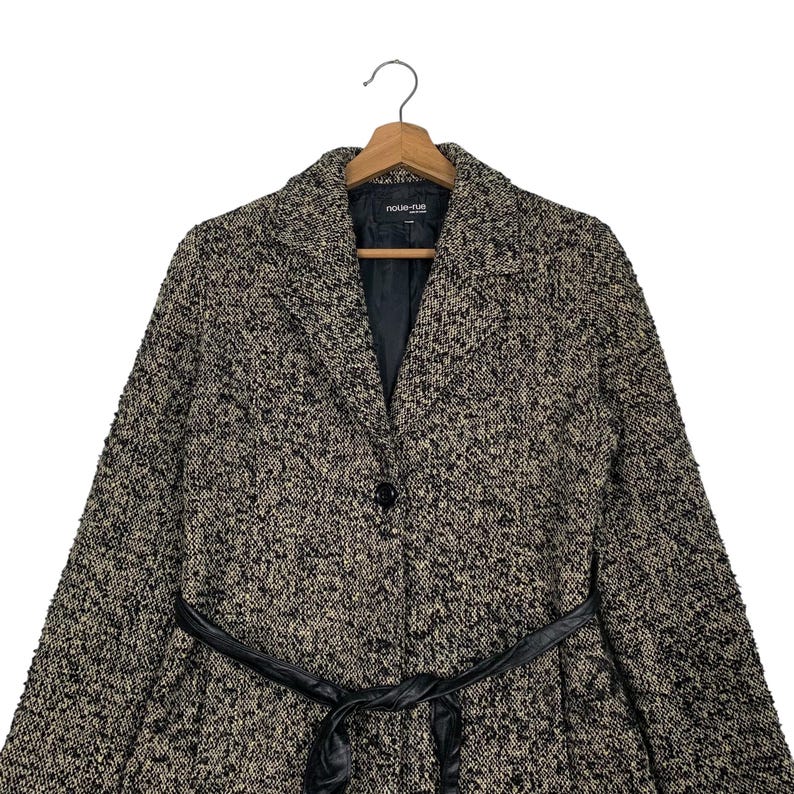 Puede incluir: Un abrigo de tweed negro y beige con cintur&oacute;n de cuero negro. El abrigo tiene cuello con solapas, cierre de un solo bot&oacute;n y el nombre de la marca "noue-rue" en la etiqueta.