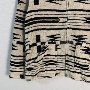 Puede incluir: Una chaqueta con cremallera de color blanco y negro con un dise&ntilde;o del suroeste. La chaqueta tiene dos bolsillos en la parte delantera.