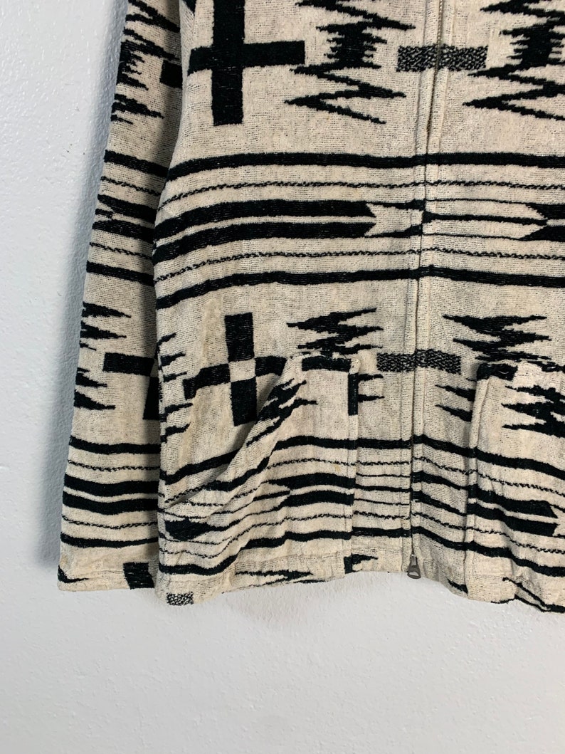 Puede incluir: Una chaqueta con cremallera de color blanco y negro con un dise&ntilde;o del suroeste. La chaqueta tiene dos bolsillos en la parte delantera.