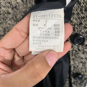 Puede incluir: Primer plano de una etiqueta de ropa con texto y n&uacute;meros japoneses. La etiqueta detalla la composici&oacute;n de la tela: 80% lana, 10% poli&eacute;ster, 5% acr&iacute;lico y 5% nailon. La etiqueta est&aacute; adherida a una tela de tweed.