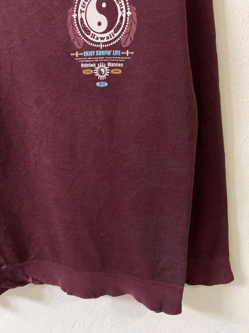 Puede incluir: Sudadera color burdeos con un estampado gr&aacute;fico de un s&iacute;mbolo yin yang con el texto "T.G.I. Fridays Hawaii" y "Enjoy Surfin' Life" con las ubicaciones "Haleiwa" y "Waimea".