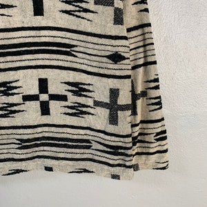 Puede incluir: Una manta tejida en blanco y negro con un patr&oacute;n geom&eacute;trico que presenta cruces y puntas de flecha.