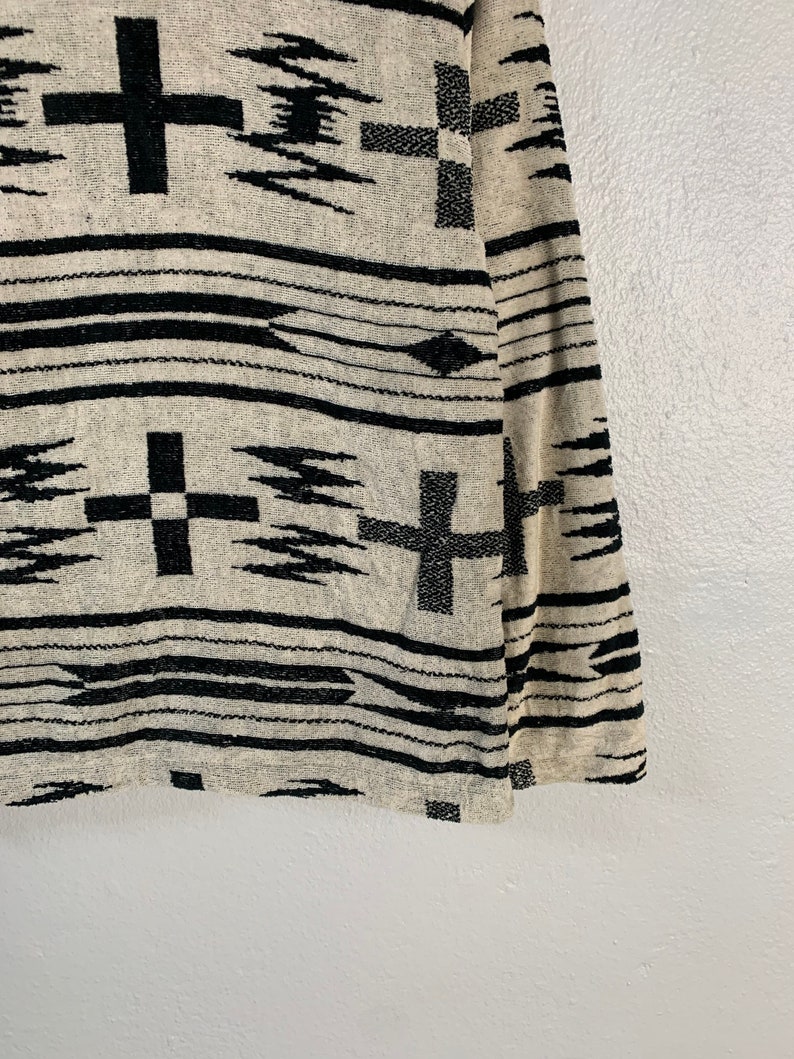 Puede incluir: Una manta tejida en blanco y negro con un patr&oacute;n geom&eacute;trico que presenta cruces y puntas de flecha.