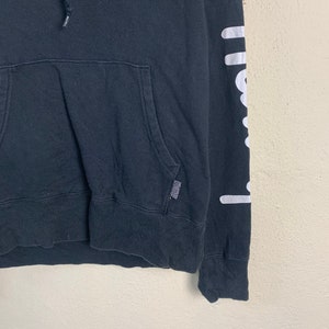 May include: Black hooded sweatshirt with white graphic print on the sleeve and a small white graphic print on the front. The print on the sleeve says "chillwave".