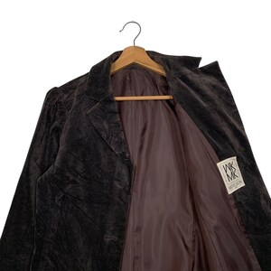 Peut inclure: Un blazer en velours marron fonc&eacute; avec un col crant&eacute; et deux boutons, suspendu &agrave; un cintre en bois. La doublure int&eacute;rieure est de couleur marron clair. Une &eacute;tiquette avec le texte "WK MK MODEL RIN" est visible.