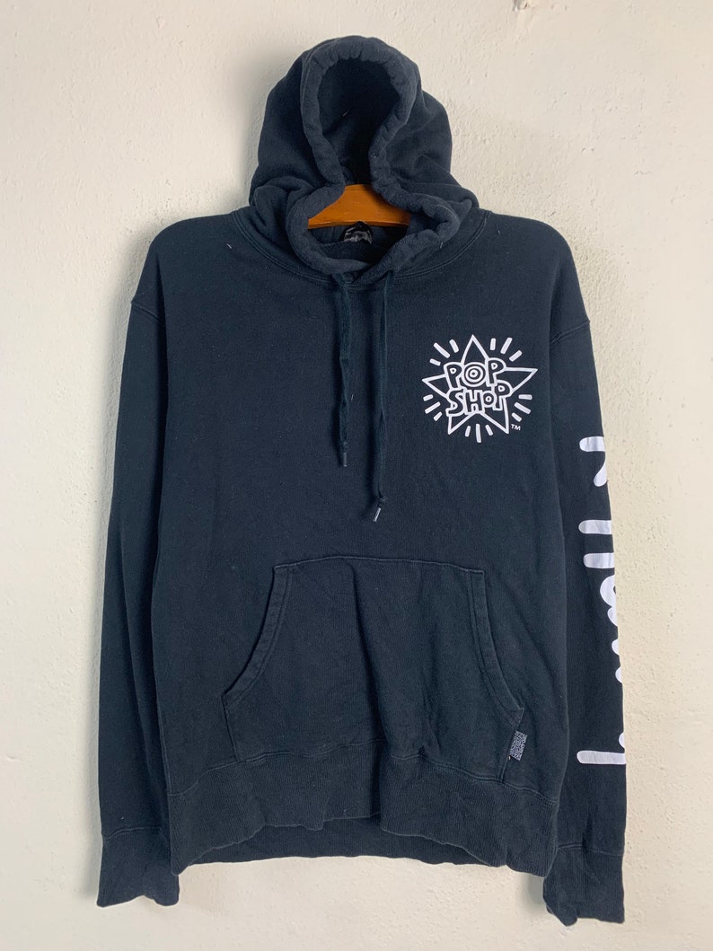 May include: Black hooded sweatshirt with a white graphic of a star with the text "POP SHOP" inside. The right sleeve has a white graphic of the word "POP" repeated vertically.