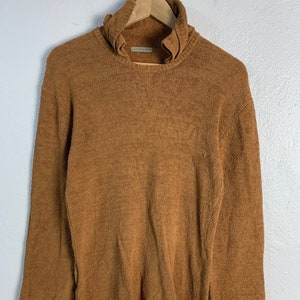 Puede incluir: Un su&eacute;ter de cuello alto marr&oacute;n con un cuello fruncido. El su&eacute;ter est&aacute; hecho de un material suave y peludo.