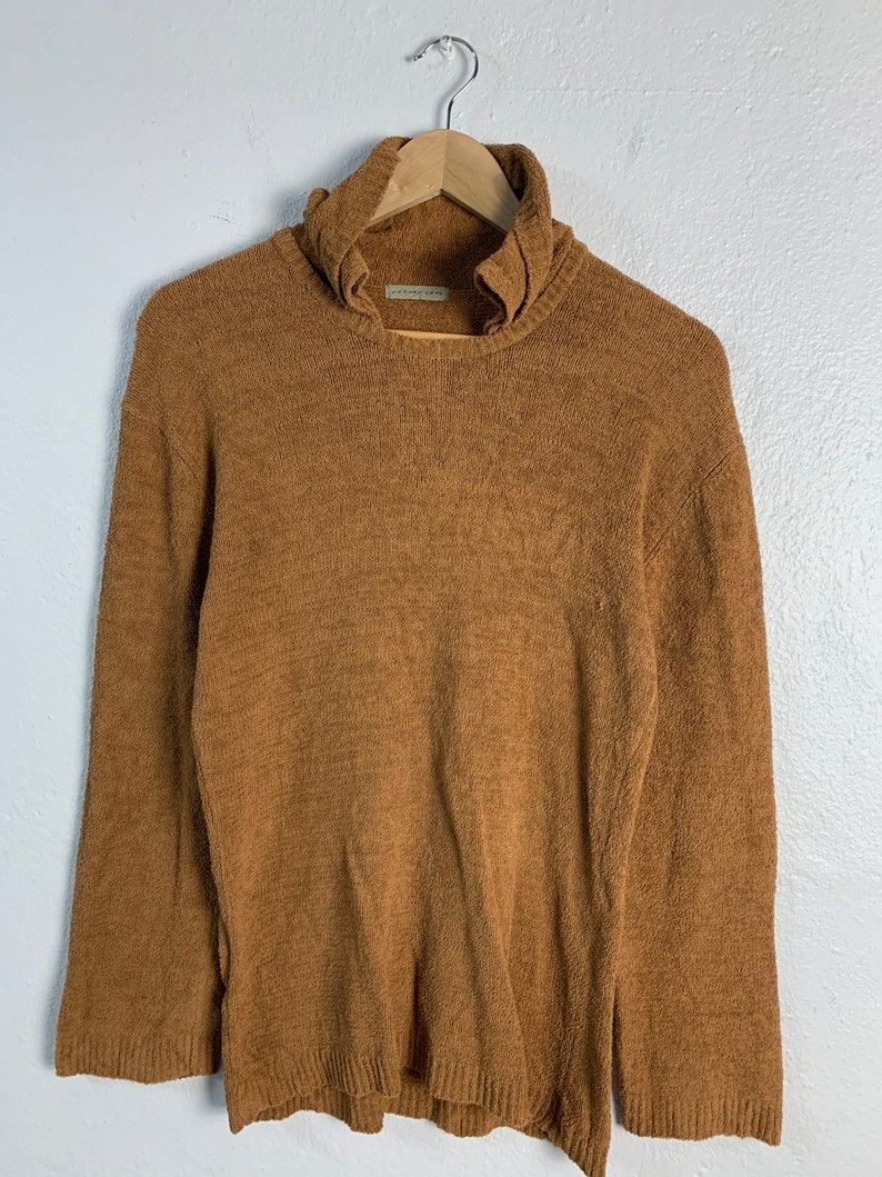 Puede incluir: Un su&eacute;ter de cuello alto marr&oacute;n con un cuello fruncido. El su&eacute;ter est&aacute; hecho de un material suave y peludo.