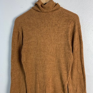 Puede incluir: Un su&eacute;ter de cuello alto marr&oacute;n con mangas largas.