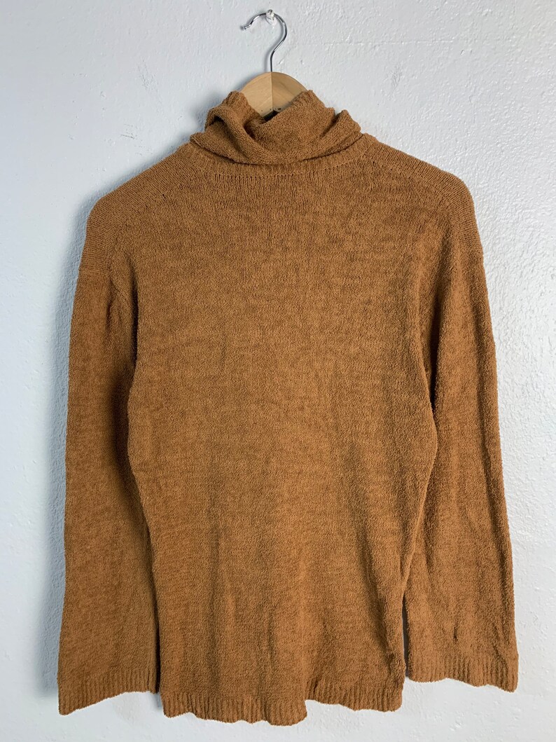 Puede incluir: Un su&eacute;ter de cuello alto marr&oacute;n con mangas largas.