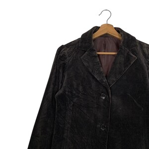 Peut inclure: Veste blazer en velours marron fonc&eacute; avec un col crant&eacute; classique et une fermeture &agrave; deux boutons. Le blazer est suspendu &agrave; un cintre en bois sur fond blanc. La veste a des manches longues et une coupe ajust&eacute;e.