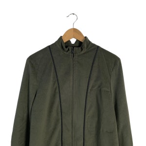 May include: A dark green zip-up jacket with black trim on the seams. The jacket is hanging on a wooden hanger.
