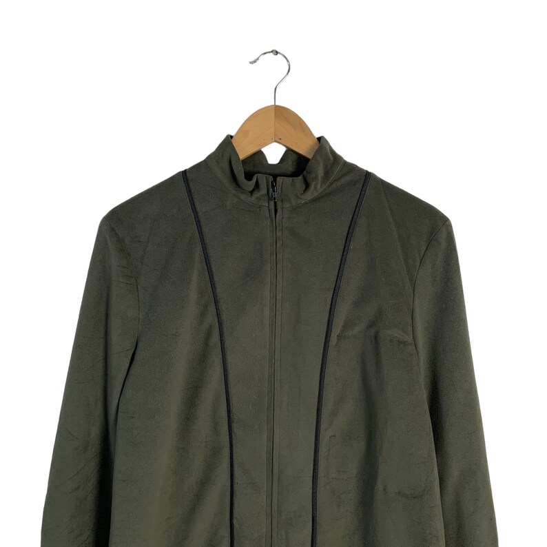 May include: A dark green zip-up jacket with black trim on the seams. The jacket is hanging on a wooden hanger.