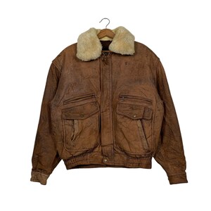 Puede incluir: Una chaqueta bomber de cuero marrón con cuello de piel sintética. La chaqueta tiene varios bolsillos y una cremallera.