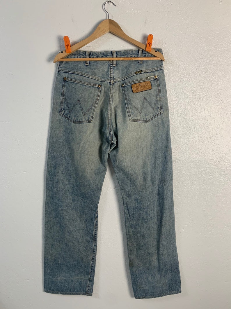 Op de afbeelding: Een lichtblauwe spijkerbroek met een bruin lederen Wrangler-label op de achterzak.