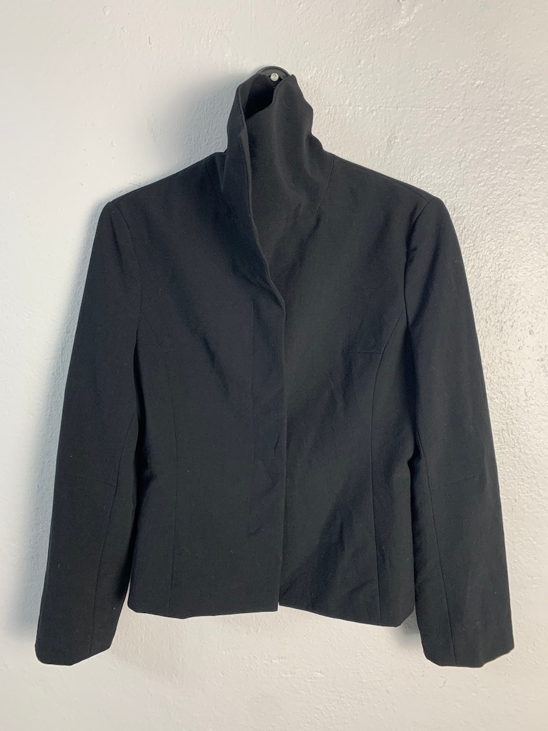 May include: A black blazer with a high, folded collar. The blazer has a single button closure and long sleeves.