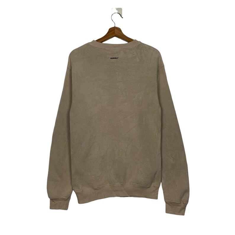 May include: A light brown sweatshirt with a crew neck and long sleeves. The sweatshirt has a small, black logo on the front.