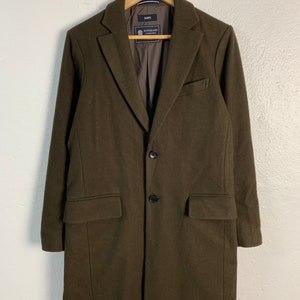 May include: A long, dark green wool coat with a single-breasted closure and two button pockets. The coat has a label that reads "SHIPS" and "SUPERIOR" in black text.