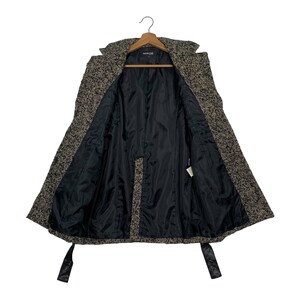 Puede incluir: Abrigo de tweed abierto con forro negro. El abrigo est&aacute; colgado de una percha de madera. Tiene cuello con solapas, mangas largas y cintur&oacute;n anudado. La tela exterior es una mezcla de hilos negros, marrones y blancos.