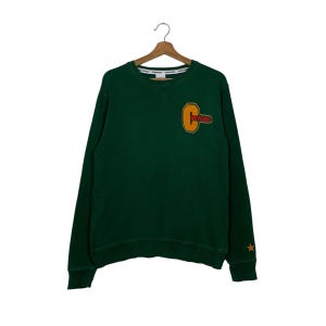 May include: A green long-sleeved sweatshirt with a large yellow and red "Converse" logo on the front. The sweatshirt has a star on the left sleeve.