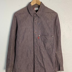 May include: A long-sleeved, brown button-down shirt with a single chest pocket and a Levi's logo on the pocket. The shirt has a subtle herringbone pattern.