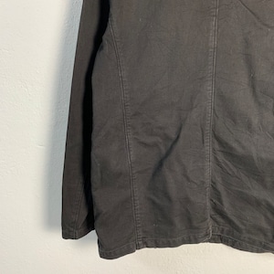 Puede incluir: Primer plano de una chaqueta negra. La chaqueta tiene un dise&ntilde;o a medida con costuras visibles y una silueta estructurada. La tela parece ser un material resistente, posiblemente algod&oacute;n o una mezcla, con una superficie ligeramente texturizada.