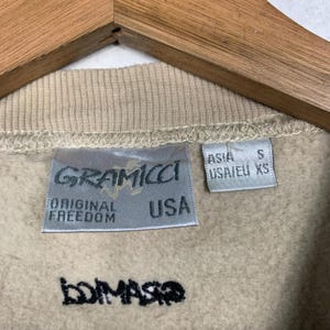 May include: A beige sweatshirt with a Gramicci label that says "Original Freedom USA" and a size tag that says "Asia S USA/EU XS". The sweatshirt also has the word "bompasso" written in black on the front.